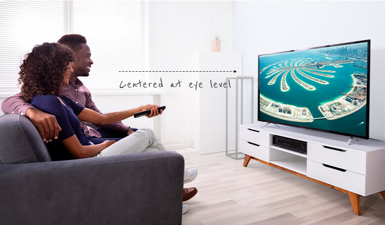 Male and female sitting on grey couch watching TV together, women holding the TV remote